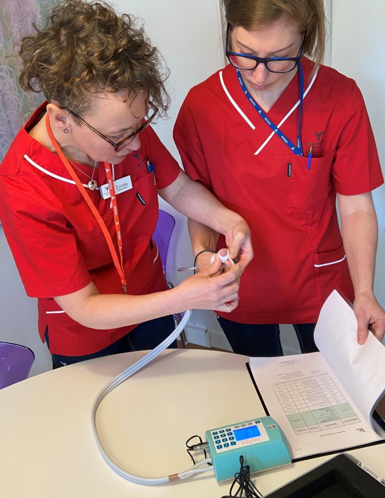 Sjuksköterskorna Lovisa Åhlin Billeskalns och Louise Raihle Lagnecranz och går igenom tåtrycksmätaren (men visar här på tummen istället för tån). Bild: Privat