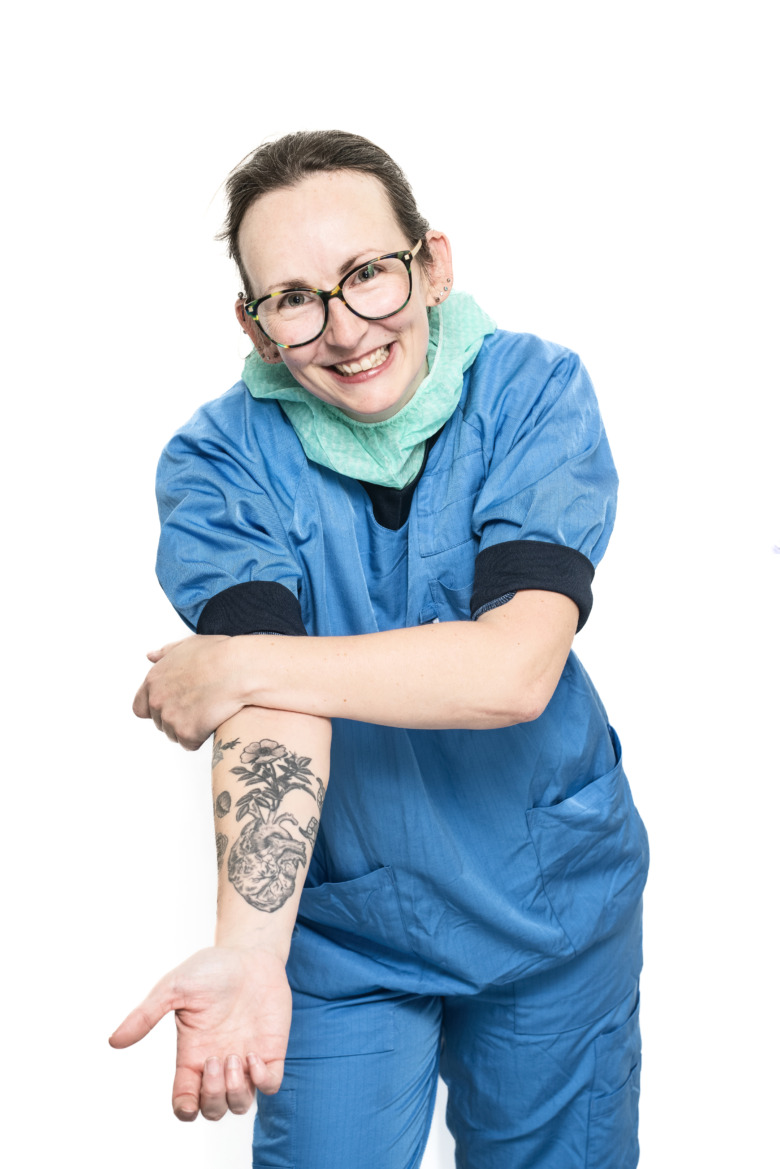 Helen Granlund, röntgensjuksköterska, iklädd blå arbetskläder visar upp insidan på sin ena arm där hon har en stor tatuering i form av ett hjärta som det växer blommor ur