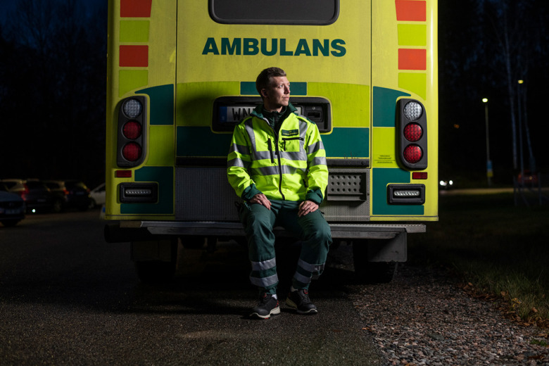 Elias Hedlund blickar ifrån kameran medan han sitter på en utstickande kant på baksidan av ambulansen