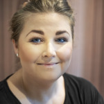 Porträtt av Maria Lindblom som är vice ordförande i Vårdförbundet avdelning Stockholm. Hon ler, har en tofs på huvudet och en svart t-shirt. Hon sitter framför en rosa bakgrund.