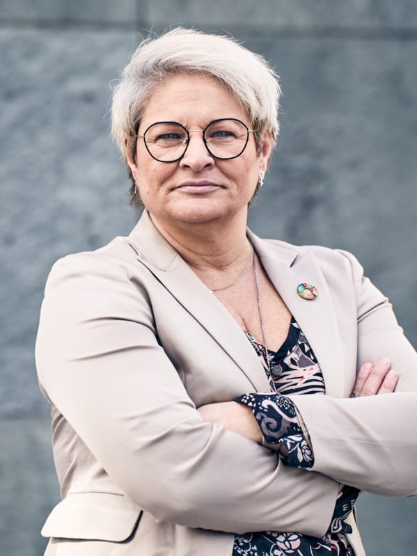 Sineva Ribeiro, ordförande Vårdförbundet, står med armarna i kors vid en grå stenvägg.