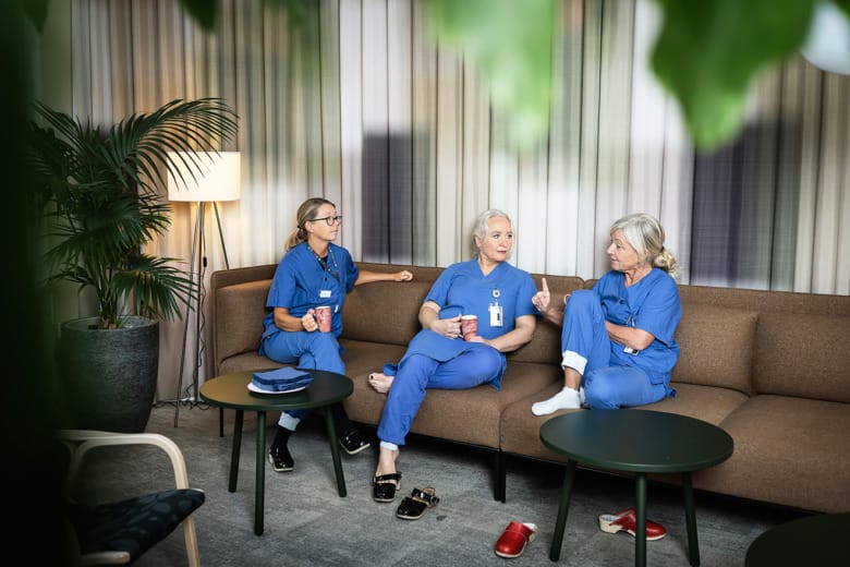 Ultraljudsbarnmorskan Christina Nyberg Österstrom sitter i en brun soffa tillsammans med två kollegor på vardera sida. De har alla uppsatt hår och är iklädda blå arbetskläder. De sitter avslappnade i soffan med varsin kopp i handen och pratar med varandra.