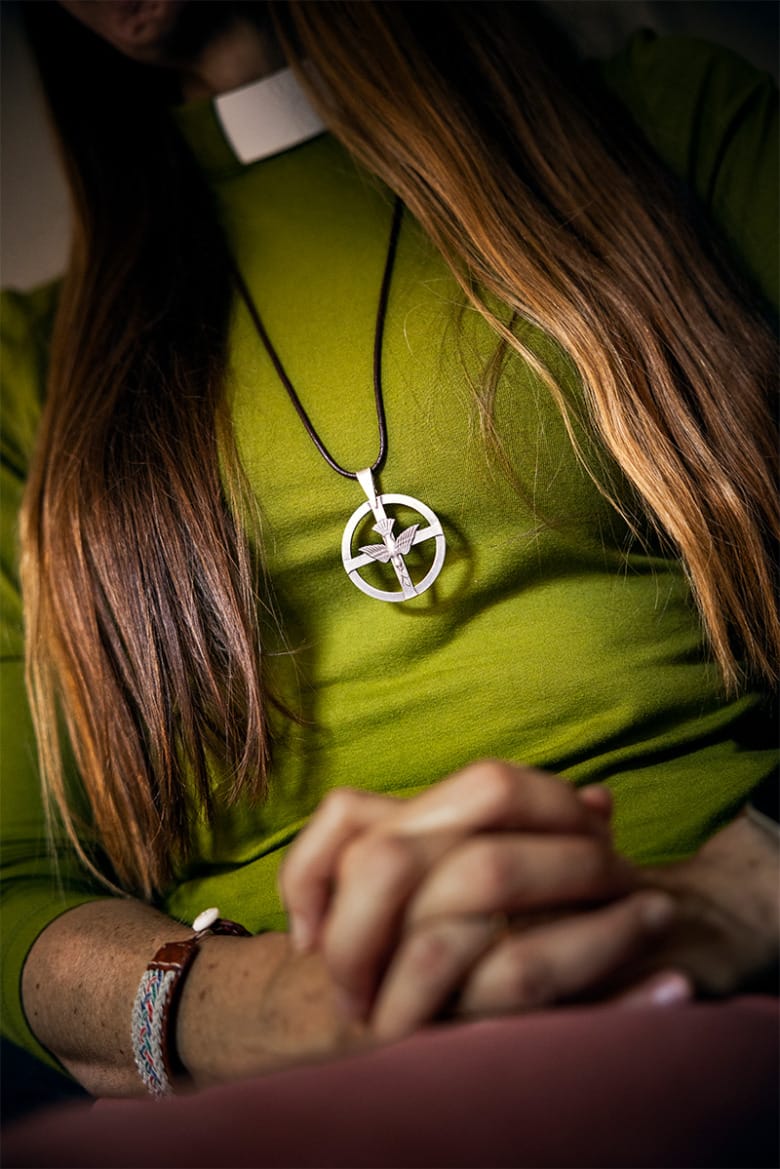 Närbild på diakonen Sara Ivarsson där bara hennes hår, överkropp och händer syns, hon bär en grön tröja och ett halsband med ett diakonemblem.