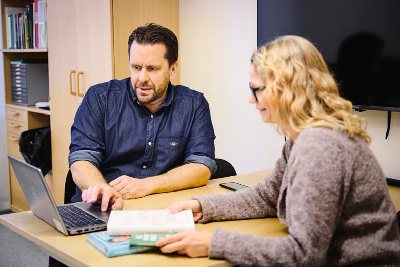 Verksamhetschef Carl-Henrik Sirkka och Sara Turtola sitter mitt emot varandra vid ett bord och tittar på en laptop som de har mellan sig.