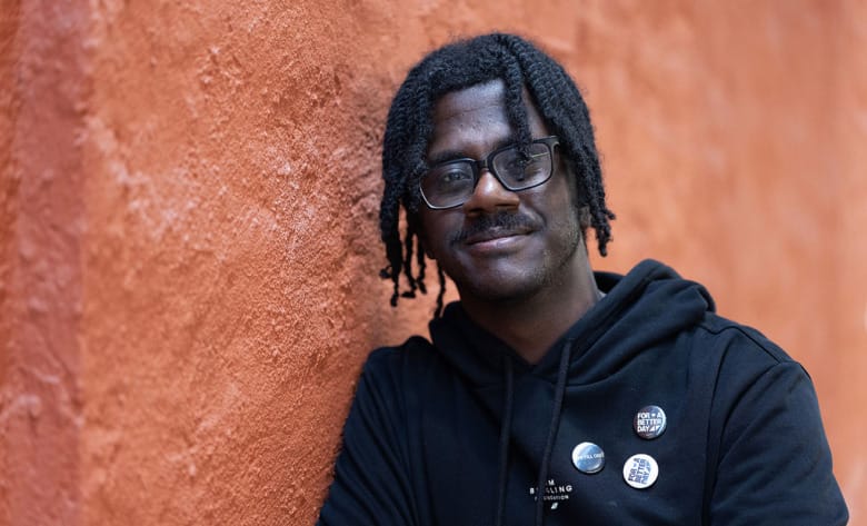 Love Runesson står lutad mot en vägg med orange puts.