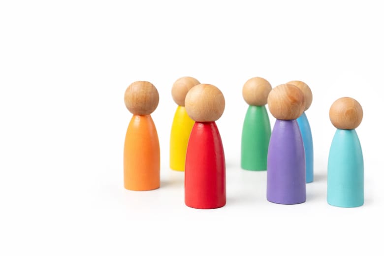 En bild på sju olikfärgade spelpjäser som liknar personer. De har varsin individuell färg på kroppen men alla har ett träfärgat huvud.