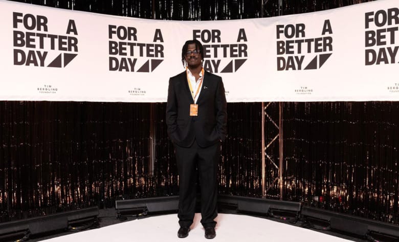 Love Runesson står iklädd svart kostym framför en svart vägg med texten "For a better day, Tim Bergling Foundation" upprepat mot en vit bakgrund