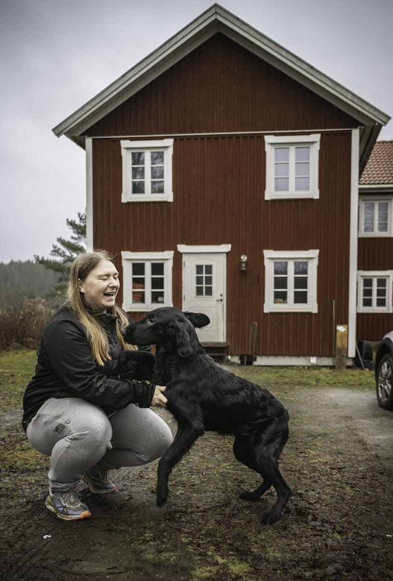 Therese van der Veer sitter på huk pch busar med sin hund utanför sitt hus.