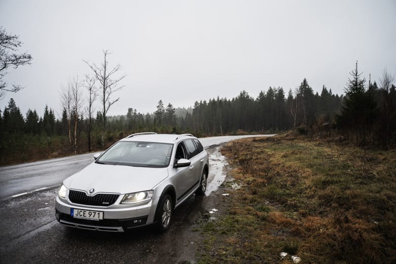 En silvrig bil står på en parkeringsficka längs med en landsväg i skogen.