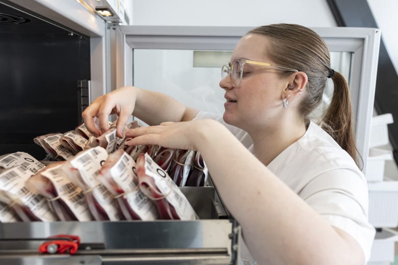 Biomedicinska analytikern Moa Hassel letar bland olika blodpåsar som ligger i en låda i ett högt skåp med öppen dörr.