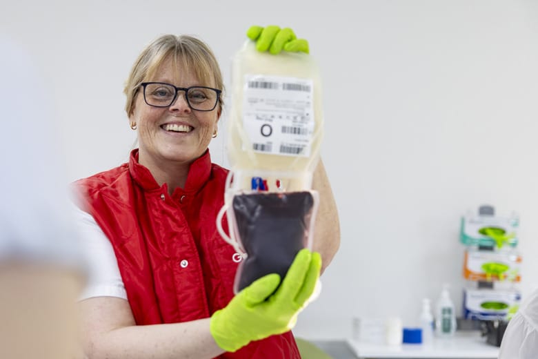 Sjuksköterskan Charlotte Ohrberg håller leendes i en blodpåse som hon visar upp för kameran.