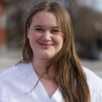 Porträtt av Elinor JOhansson. hon har ljusbrunt långt hår och bär vit bussarong.