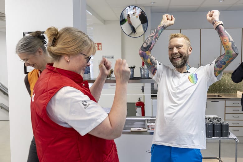 Sjuksköterskan Charlotte Ohrberg och Rickard Söderberg skrattar och höjer armarna i luften som i en segergest. I bakgrunden syns andra personer och ett kök.