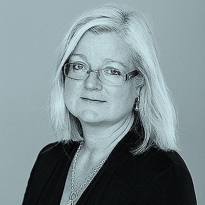 Porträtt av Carita Fallström. Hon bär glasögon, örhängen, halsband och en svart blus. Hon tittar in i kameran.