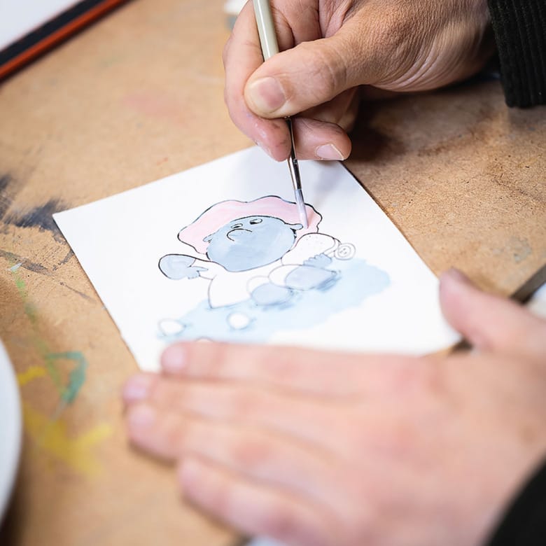 En närbild av två händer som målar en barnboksillustration.