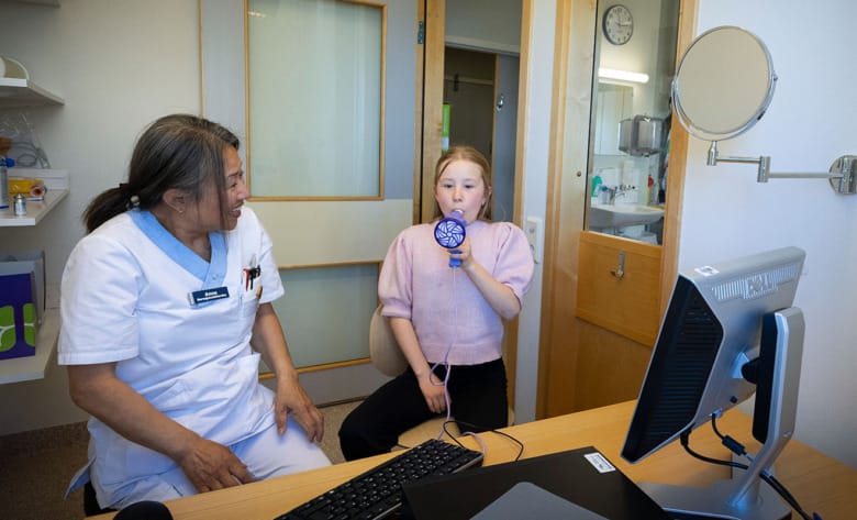 Emmy Mattsson andas i ett spirometriinstrument. Anna Lundström, sjuksköterska, tittar på.