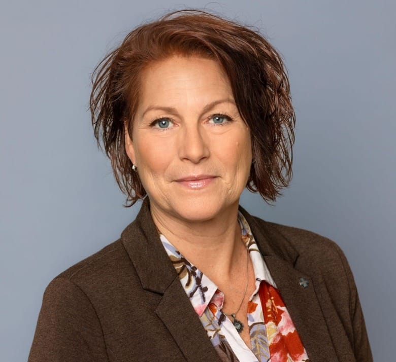 Porträtt av en kvinna med rött hår. Hon bär en blommig blus och brun kavaj.