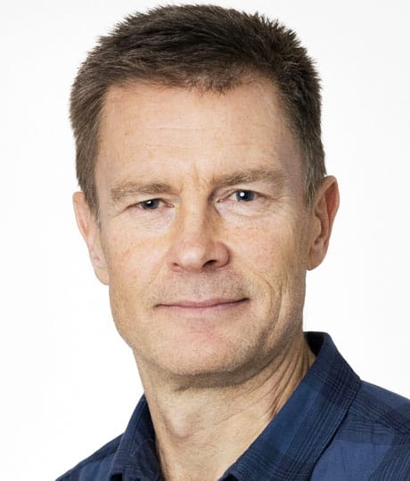 Porträtt av en man med kort brunt hår. Han bär en svart- och blårutig skjorta.