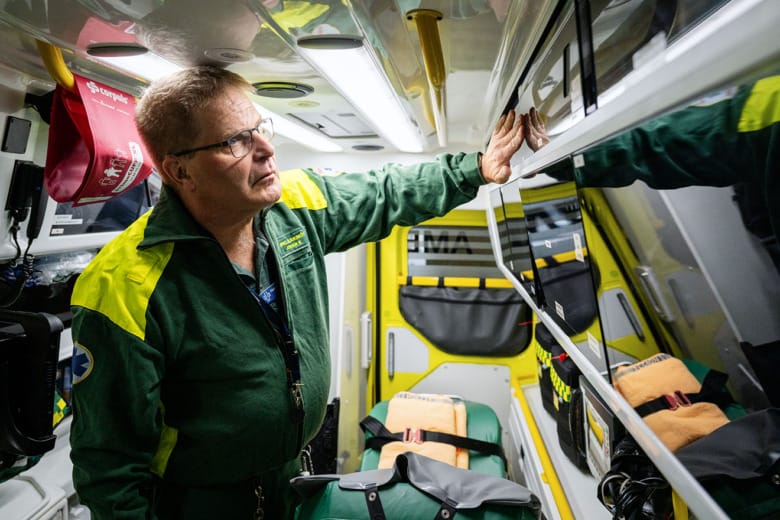 En man i gröna ambulanskläder står inne i en ambulans. Han tittar på något på en hylla nära taket.